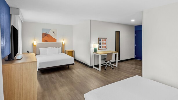A hotel room with a bed, desk, and a painting on the wall.
