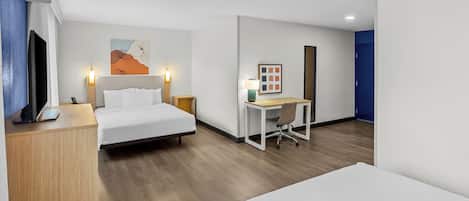 A hotel room with a bed, desk, and a painting on the wall.