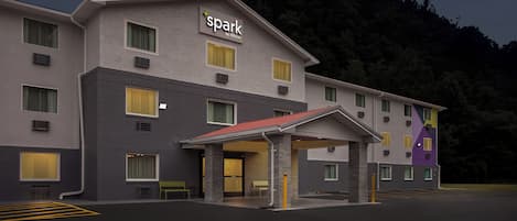 Ein Hotel mit modernem Design, das ein gut sichtbares 'Spark by Hilton'-Schild, einen überdachten Eingang und einen Parkplatz zeigt.