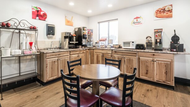 A kitchen with wooden cabinets, a round dining table with chairs, a coffee machine, and a microwave.