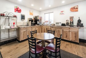 A kitchen with wooden cabinets, a round dining table with chairs, a coffee machine, and a microwave.