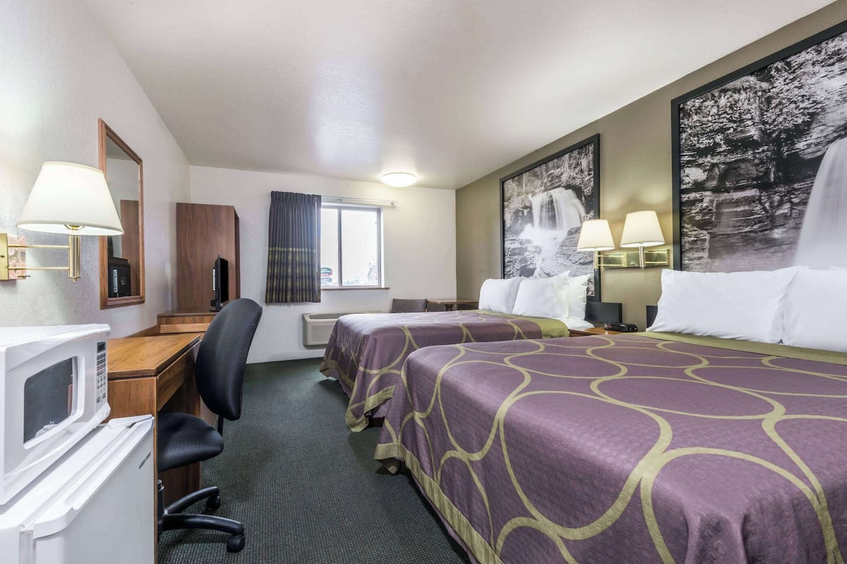A hotel room with two beds, a desk with a computer, a microwave, and a TV.