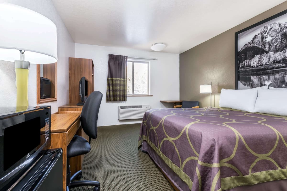 A hotel room with a bed, desk, chair, television, and a window with curtains.