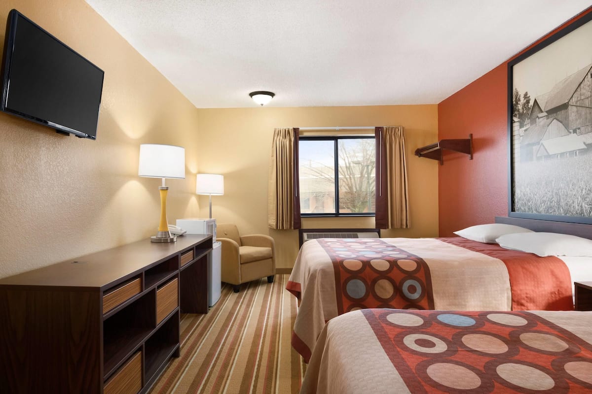 A hotel room with a bed, a desk with a lamp, a chair, a television mounted on the wall, and a window with curtains.