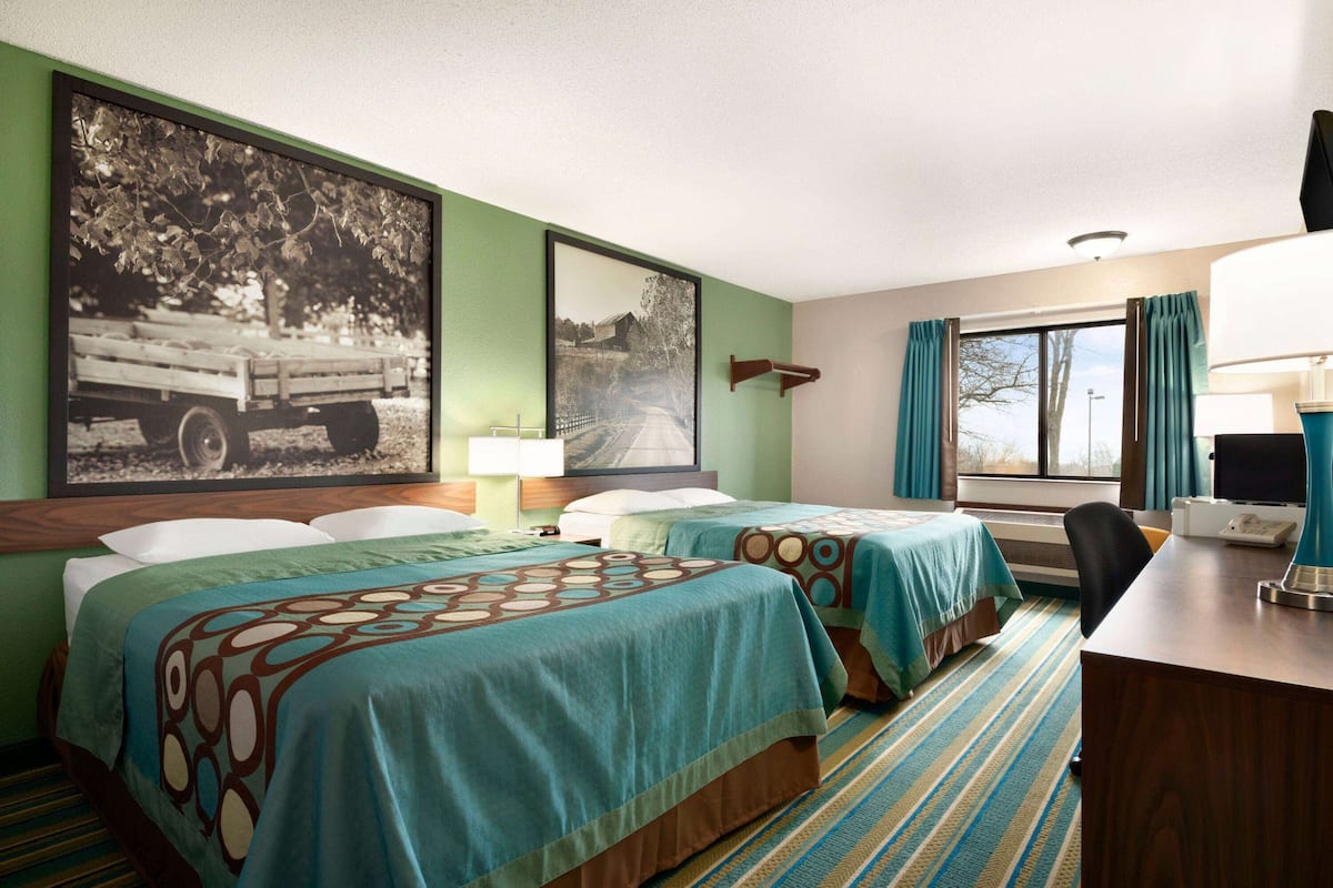 A hotel room with two beds, a desk, a chair, a lamp, and a window with curtains.