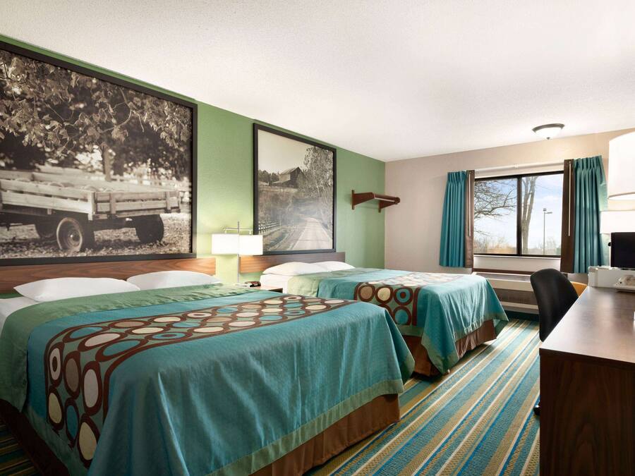 A hotel room with two beds, a desk, a chair, a lamp, and a window with curtains.