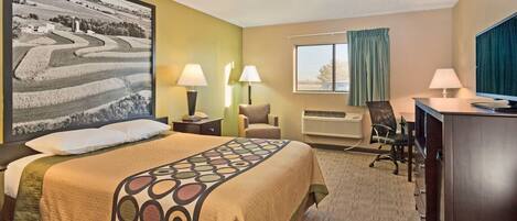 A hotel room with a bed, desk, chair, and a large landscape painting on the wall.