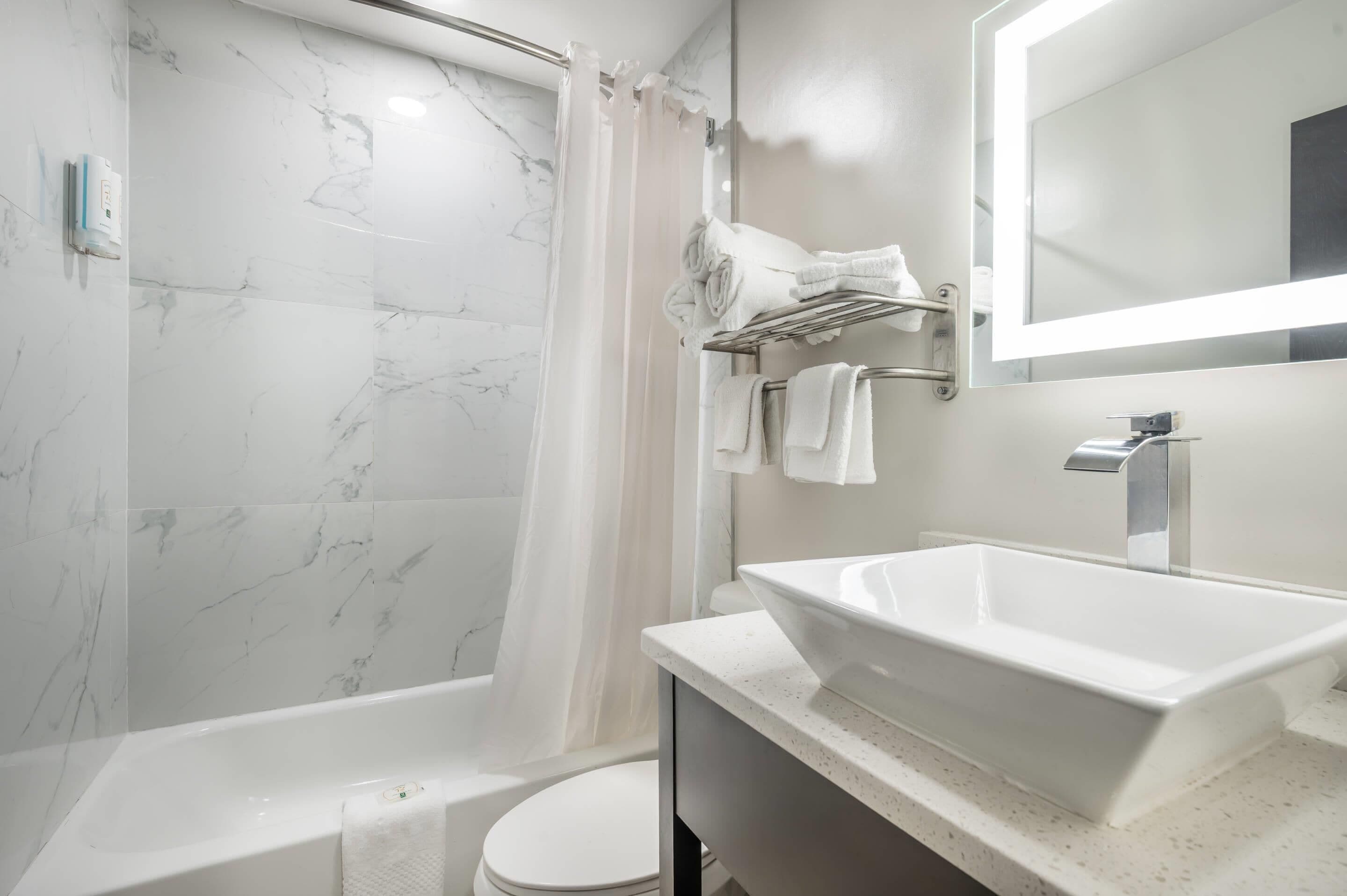 Un baño moderno con una bañera blanca, un espejo grande y un lavamanos blanco.