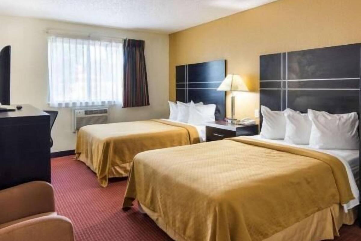 A hotel room with two beds, a desk, a chair, a TV, and a window with curtains.