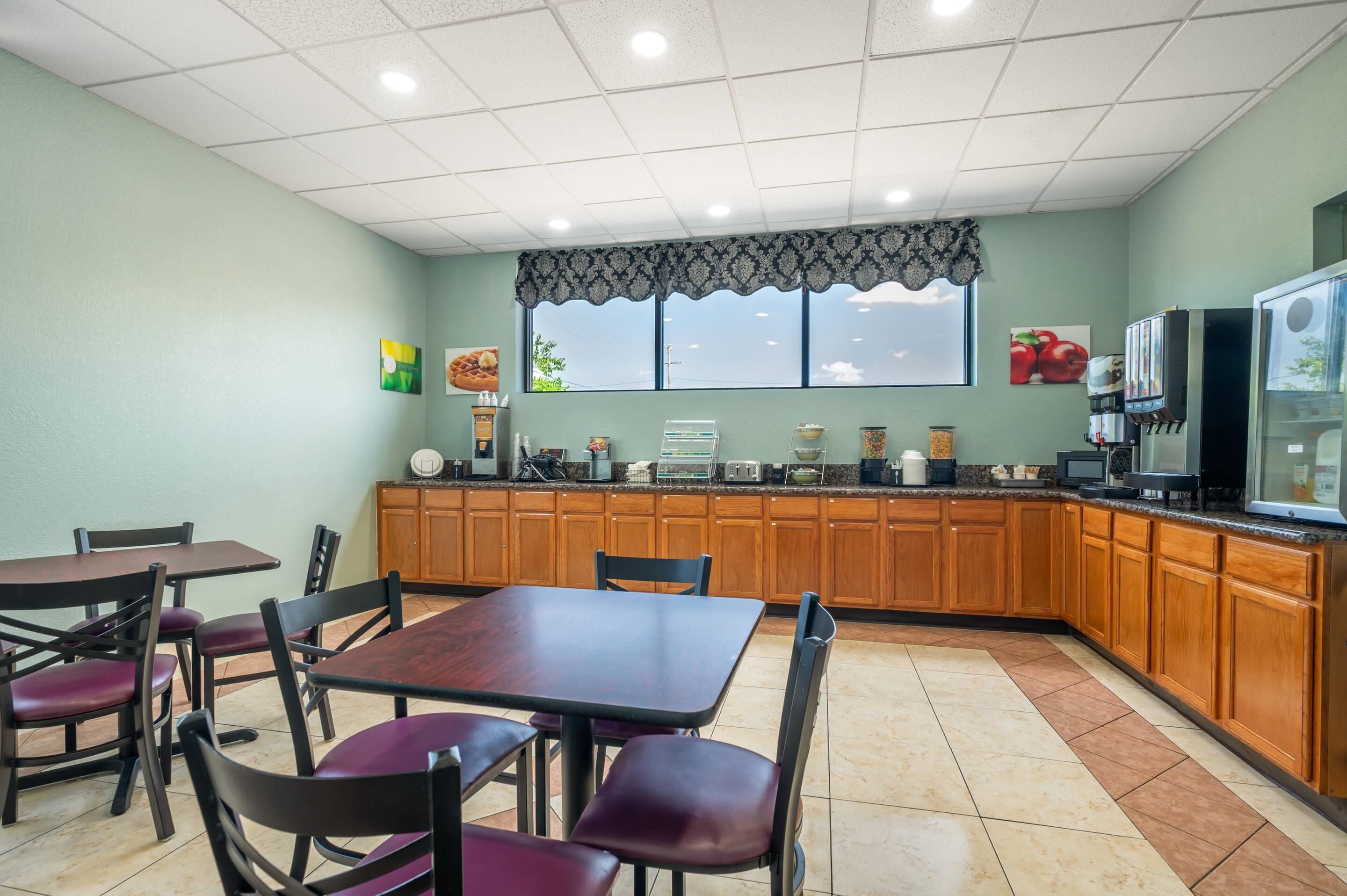 A kitchen with wooden cabinets, a dining area with tables and chairs, and a window with a view.