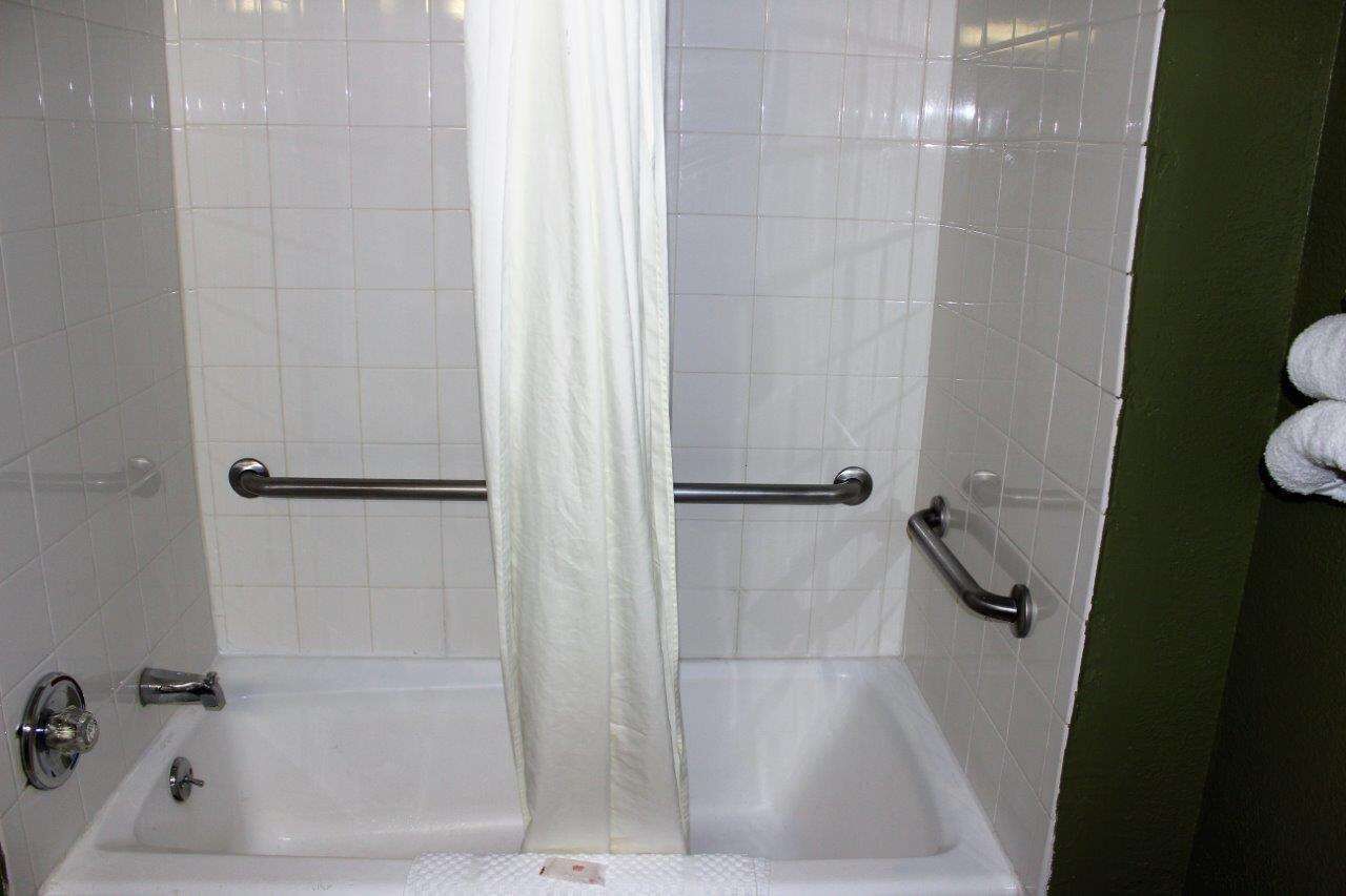 Un baño con paredes de azulejos blancos, una bañera y una cortina de ducha.