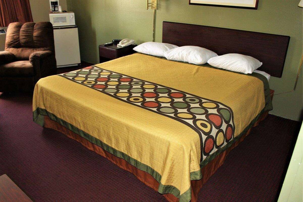 Quarto de hotel com cama, cadeira, mesa de cabeceira, telefone e micro-ondas.