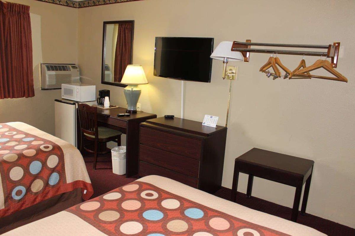 Quarto de hotel com duas camas, uma escrivaninha com cadeira, televisão, candeeiro, cabideiro e uma mesinha.