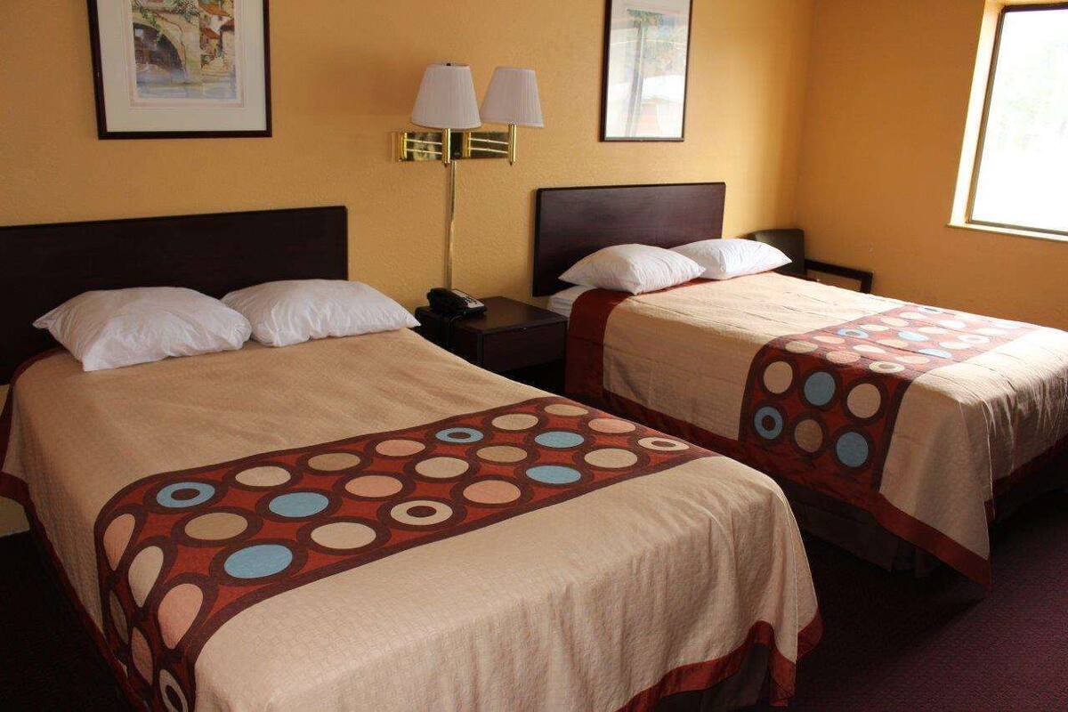 Quarto de hotel com duas camas, cada uma com colcha estampada, mesa de cabeceira com abajur e quadros nas paredes.