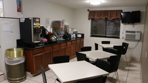 A small, clean kitchen with a refrigerator, coffee machine, and a trash can. There are two tables and chairs, and a window with blinds. - Super 8 by Wyndham San Antonio/I-35 North (San Antonio)