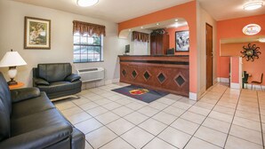 A hotel lobby with a reception desk, a black leather sofa, a lamp, and a framed picture on the wall. - Super 8 by Wyndham San Antonio/I-35 North (San Antonio)