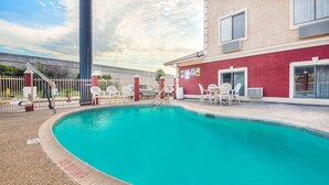 A swimming pool with a tiled deck, surrounded by a fence and white chairs. - Super 8 by Wyndham San Antonio/I-35 North (San Antonio)