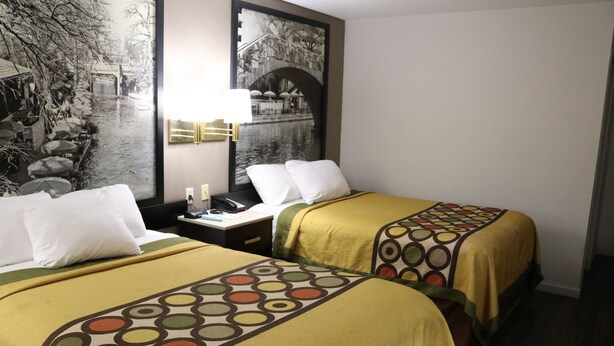 A hotel room with two beds, a nightstand, a lamp, and a large wall painting. - Super 8 by Wyndham San Antonio/I-35 North (San Antonio)