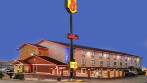 A Super 8 hotel with a 'Free Breakfast' sign, a parking lot, and a building with multiple windows and balconies. - Super 8 by Wyndham San Antonio/I-35 North (San Antonio)