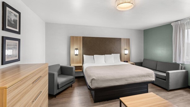 A modern hotel room with a large bed, two sofas, a wooden dresser, and a small table. - Quality Inn Atlanta Airport - Central (College Park)