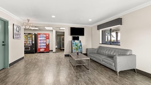 A lobby with a grey leather sofa, a coffee table, a vending machine, and a television mounted on the wall. - Quality Inn Atlanta Airport - Central (College Park)