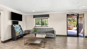 A modern lobby with a grey sofa, a coffee table, a TV, and a vending machine. - Quality Inn Atlanta Airport - Central (College Park)