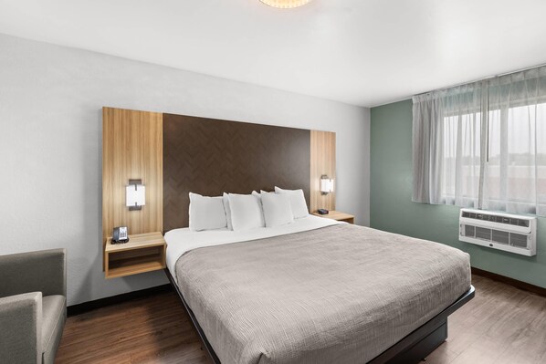 A hotel room with a large bed, a wooden headboard, bedside lamps, a small table, and a window with curtains.