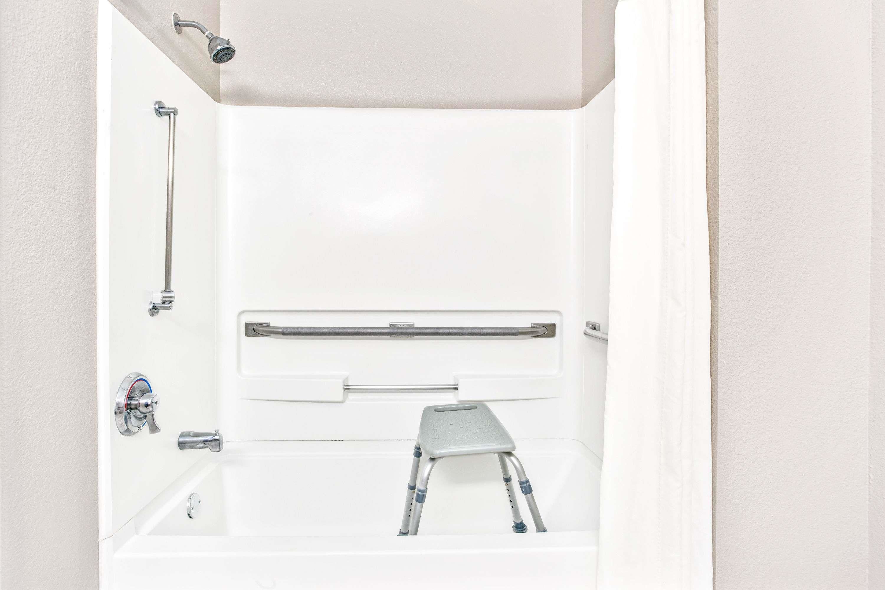 A white bathroom with a shower, grab bar, and a small step stool.