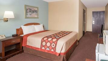 A hotel room with a bed, a nightstand, a lamp, a painting on the wall, and a door.