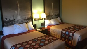 A hotel room with two beds, each with a cityscape poster, a nightstand with a lamp, and a patterned bedspread.