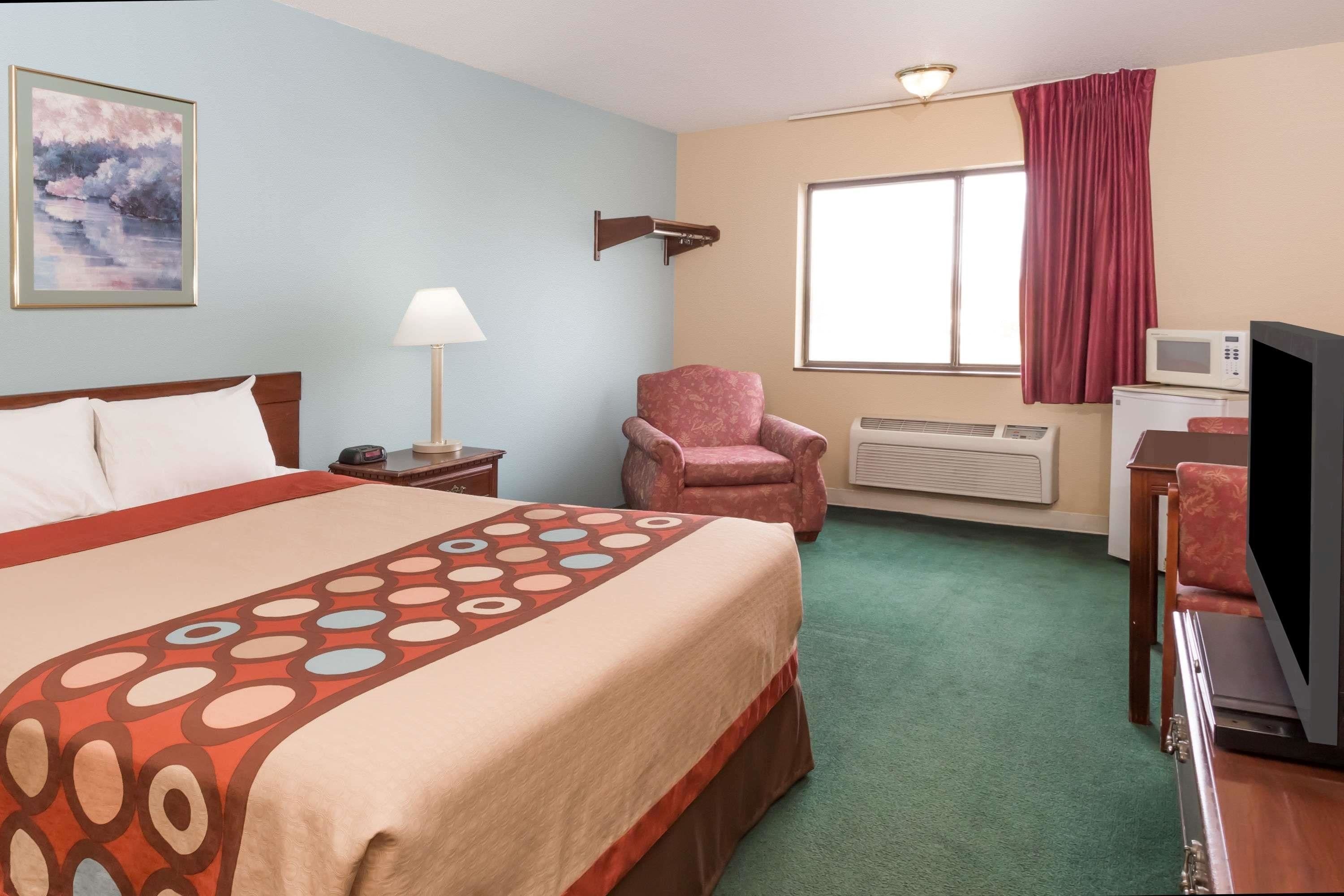 Habitación de hotel con cama, una silla, televisor, microondas y ventana con cortinas.