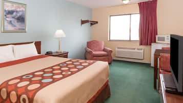 Habitación de hotel con cama, una silla, televisor, microondas y ventana con cortinas.