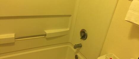 Un baño con bañera, inodoro y estante con artículos de aseo.