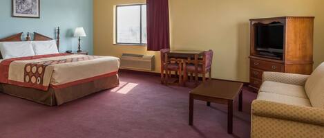 A hotel room with a bed, a desk, a television, a sofa, and a window with curtains.