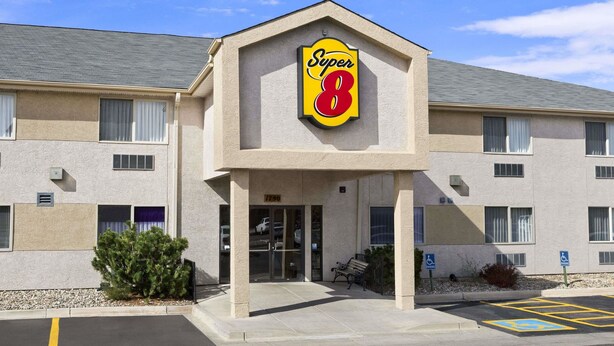 Un hotel Super 8 con fachada color beige, un llamativo letrero de 'Super 8' y un estacionamiento con espacios reservados para discapacitados.