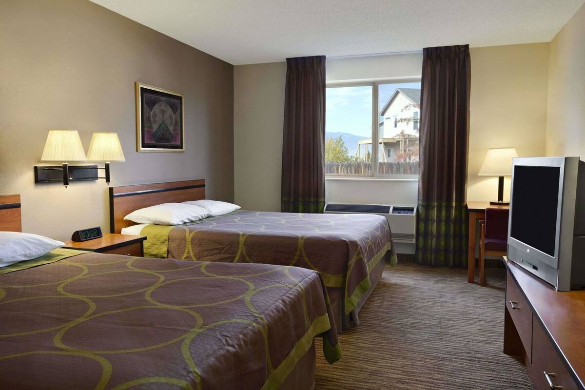 A hotel room with two beds, a TV, a desk, and a window with curtains.