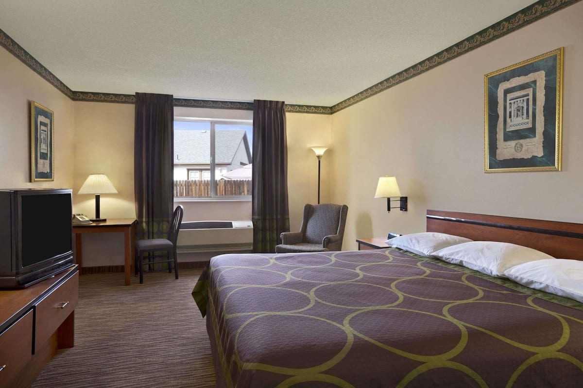 Een hotelkamer met een bed, een bureau met lamp, een stoel, een televisie en een raam met gordijnen.