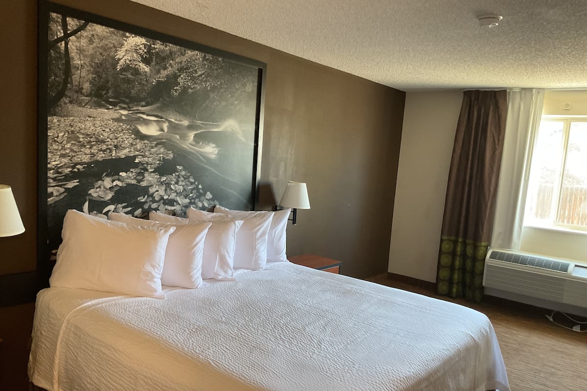 Een hotelkamer met een groot bed, twee bedlampen, een wandairconditioner en een raam met gordijnen.