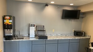Una cocina con cafetera, microondas y televisor montado en la pared.