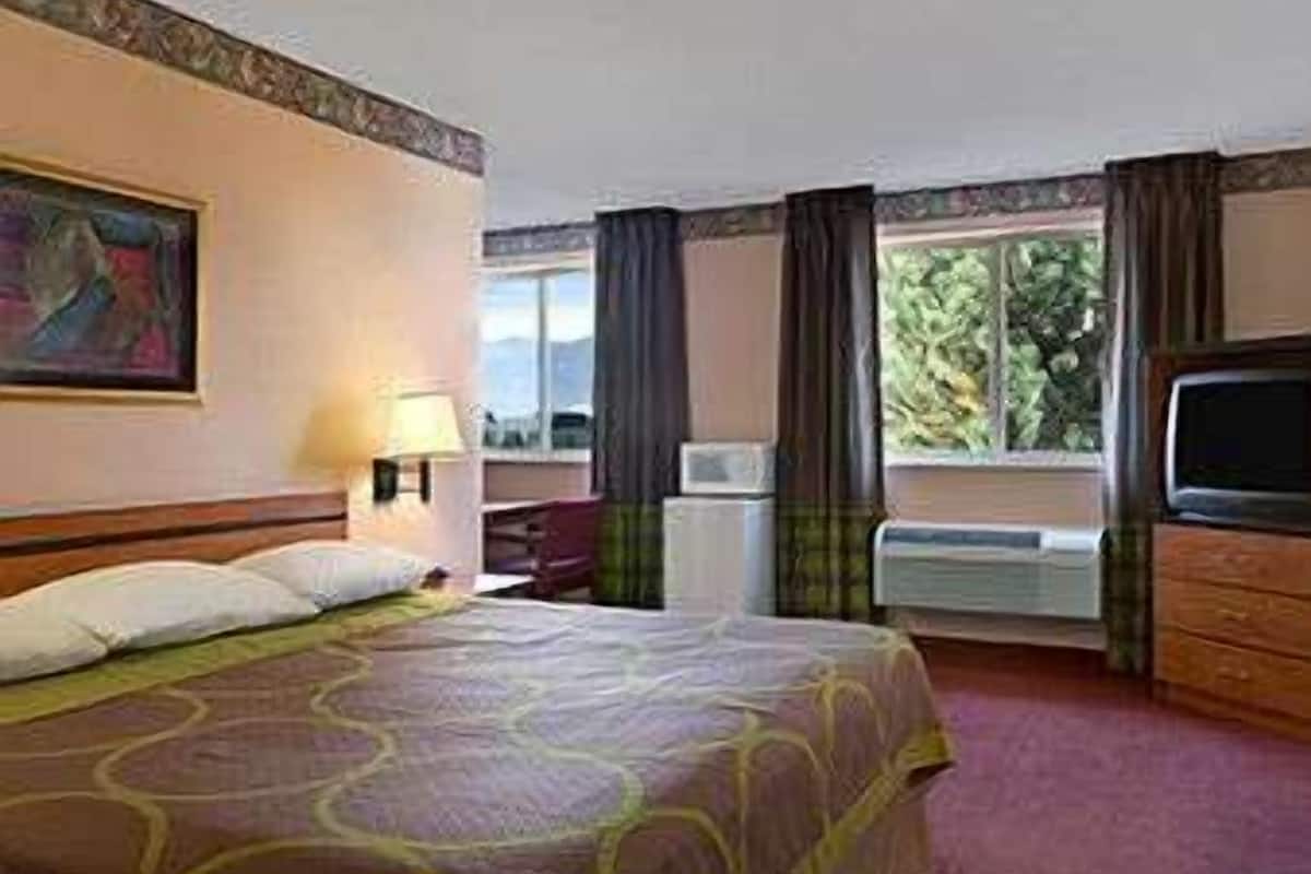 Hotelkamer met een bed, bureau, stoel, televisie en raam met gordijnen.