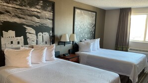 Habitación de hotel con dos camas, una mesita de noche, una lámpara y un cuadro grande en la pared.