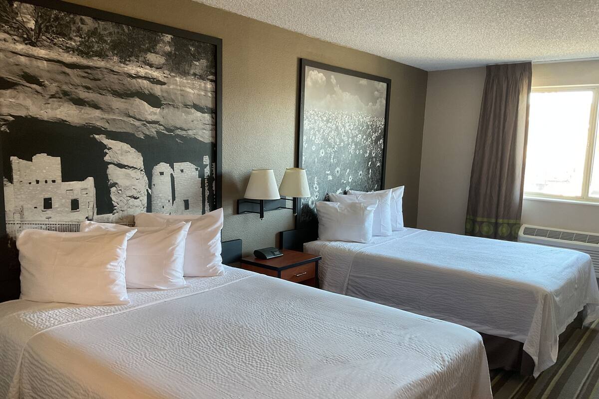 A hotel room with two beds, a nightstand, a lamp, and a large painting on the wall.