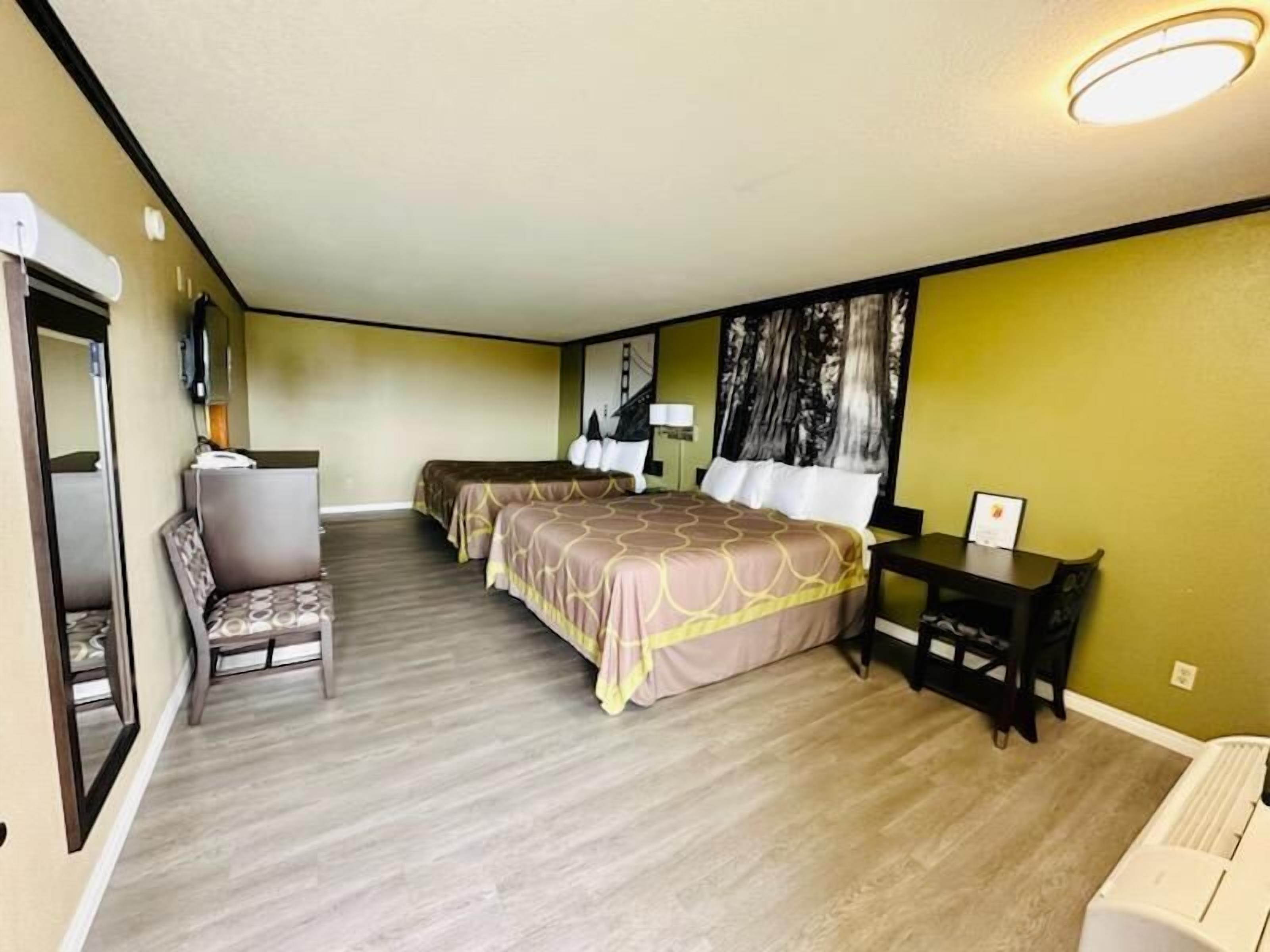 A hotel room with two beds, a desk, a chair, and a large window.