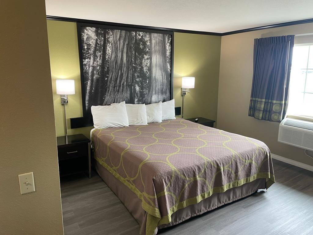 A hotel room with a large bed, two bedside tables, a wall-mounted TV, and a window with curtains.