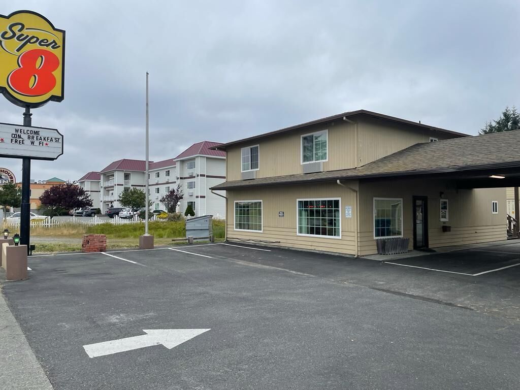Un motel Super 8 con un estacionamiento, un edificio de fachada color beige y un cielo despejado.