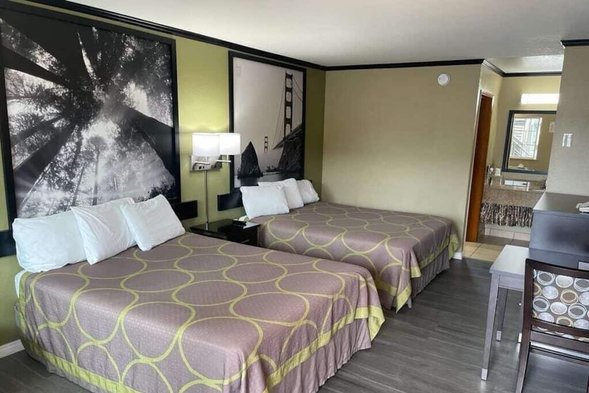 A hotel room with two beds, a desk, and a large wall mural.
