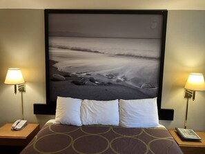 A hotel room with a bed, two bedside lamps, a telephone, and a framed photograph of a beach scene.