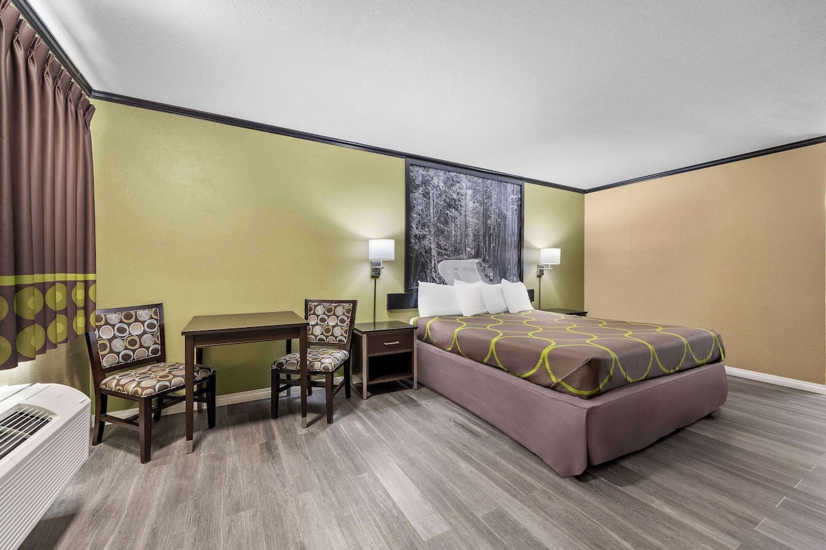 A hotel room with a bed, two chairs, a desk, and a nightstand.