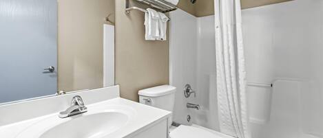 A bathroom with a white sink, toilet, and bathtub. There is a towel rack above the sink and a shower curtain.