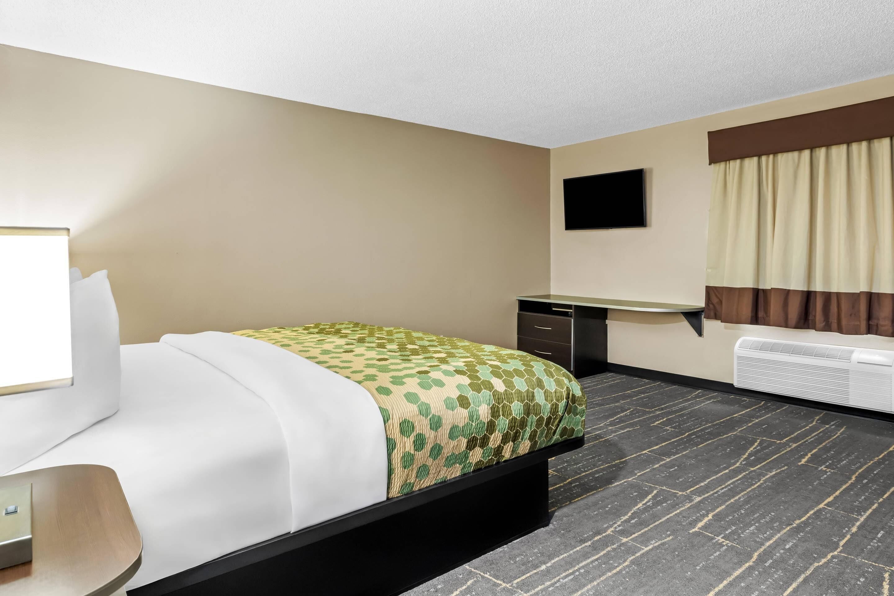 Hotelkamer met een bed, bureau, stoel, flatscreen televisie, verwarming en een raam met gordijnen.
